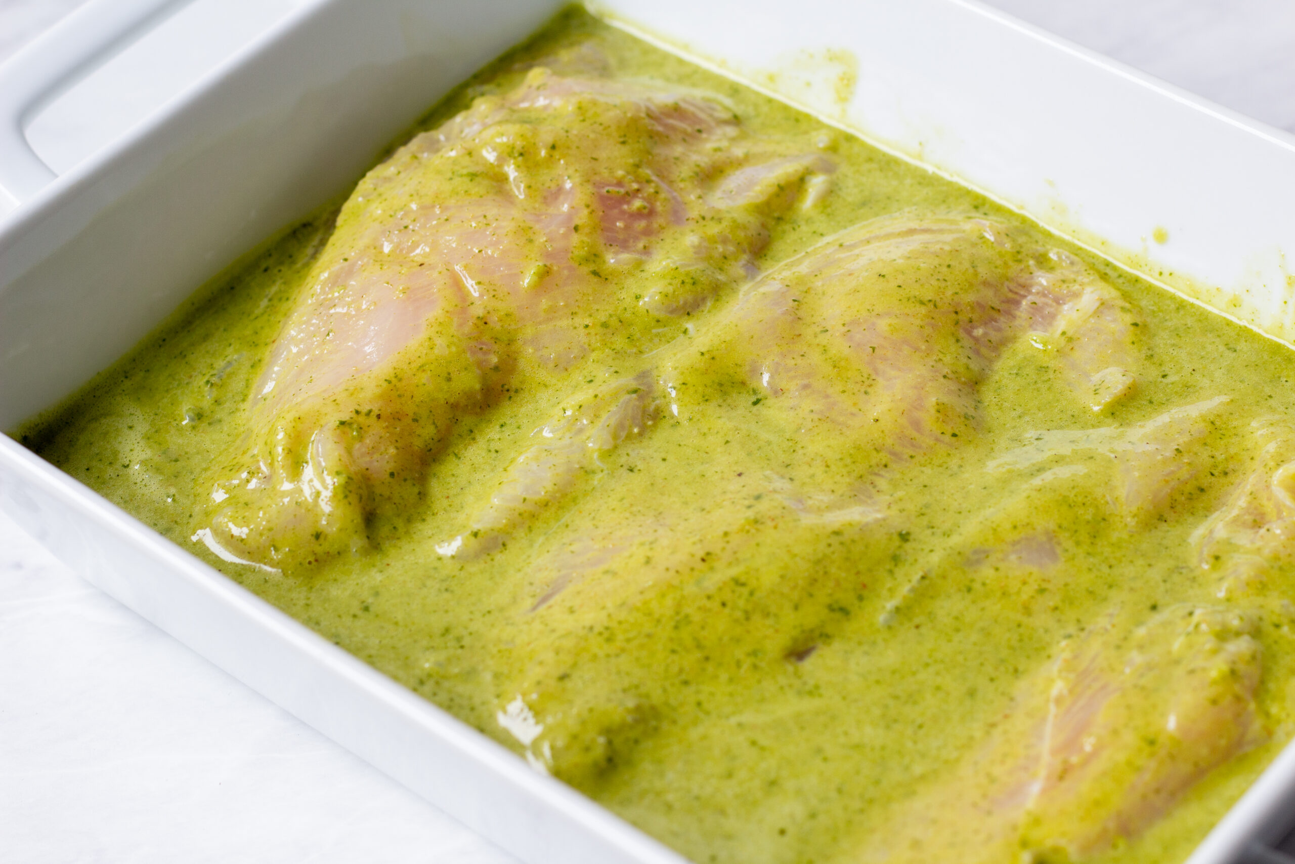 chicken breasts in a shallow white pan with bright green cilantro pepper marinade