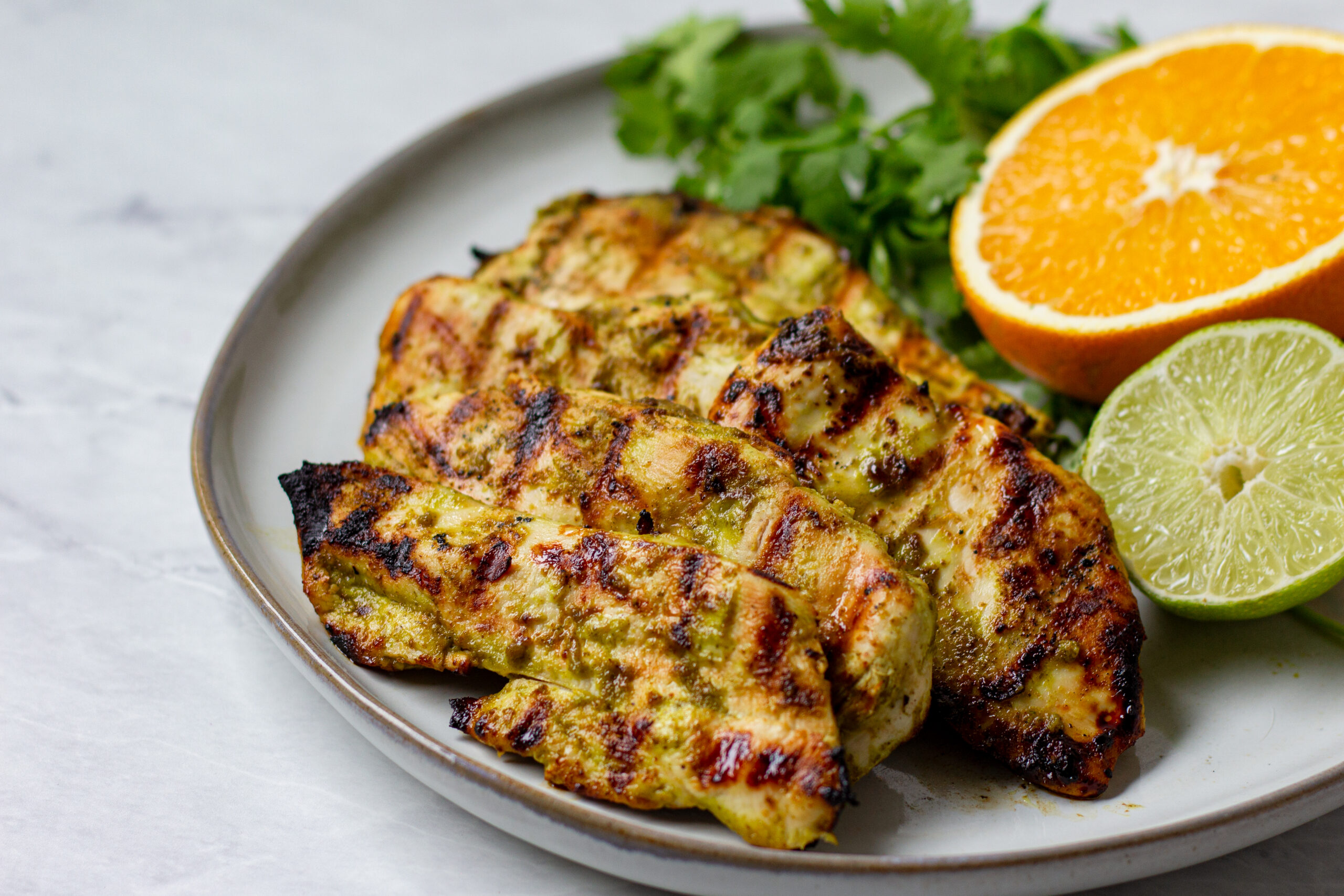 grilled chicken breasts with a bunch of cilantro sprigs orange and lime