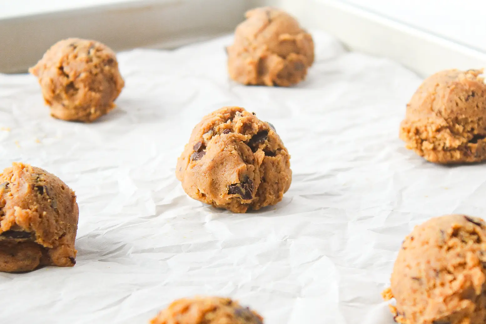 Scoops of einkorn chocolate chip cookie dough on a baking sheet with parchment paper