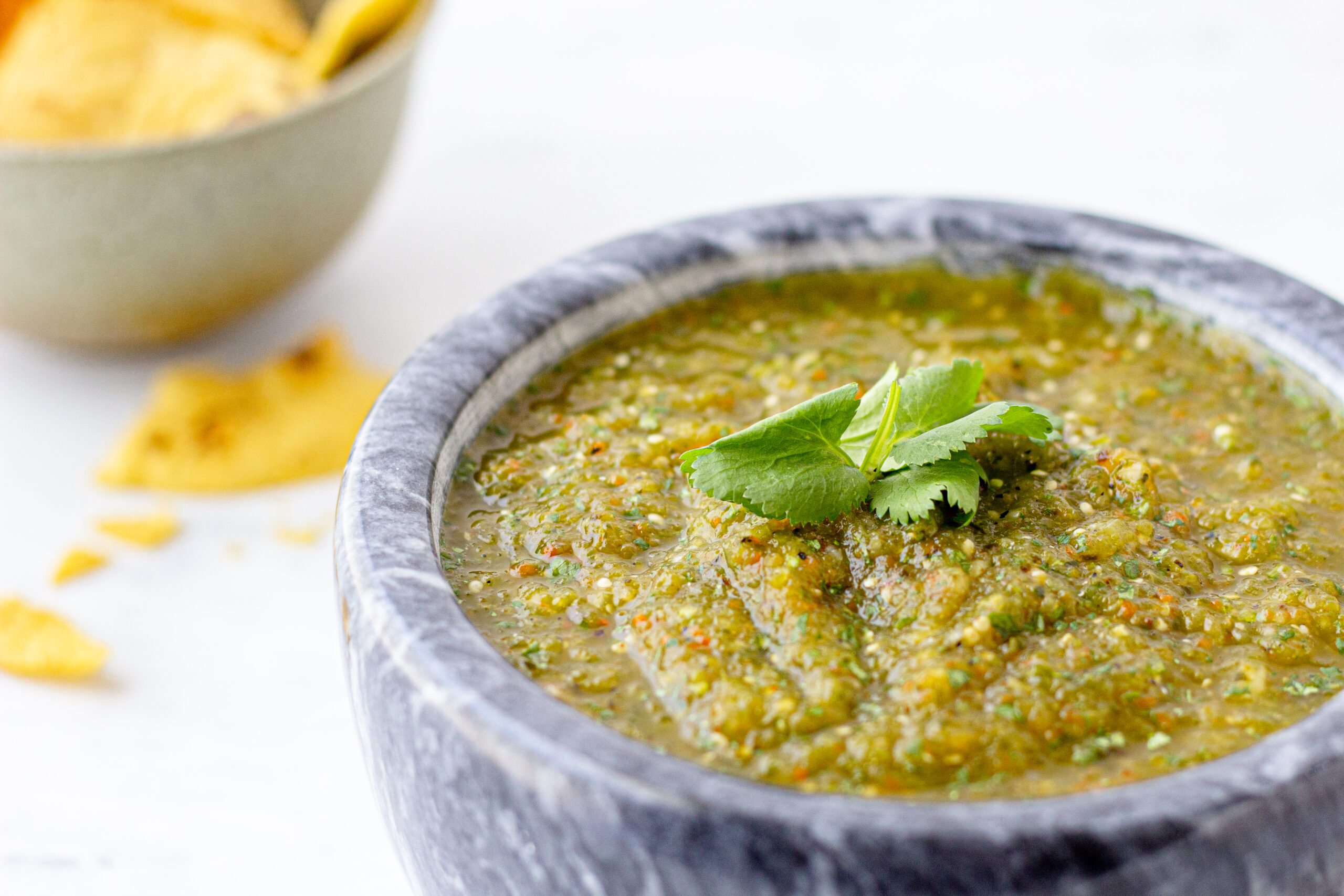verde salsa in a molcajate and sprig of cilantro on top with a bowl of tortilla chips to the side