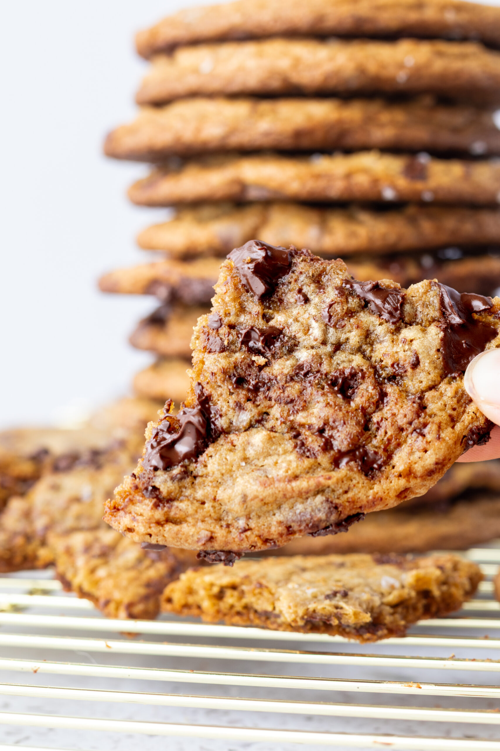 a piece of chocolate chip cookie being held for a closeup with a stack of cookies in the background
