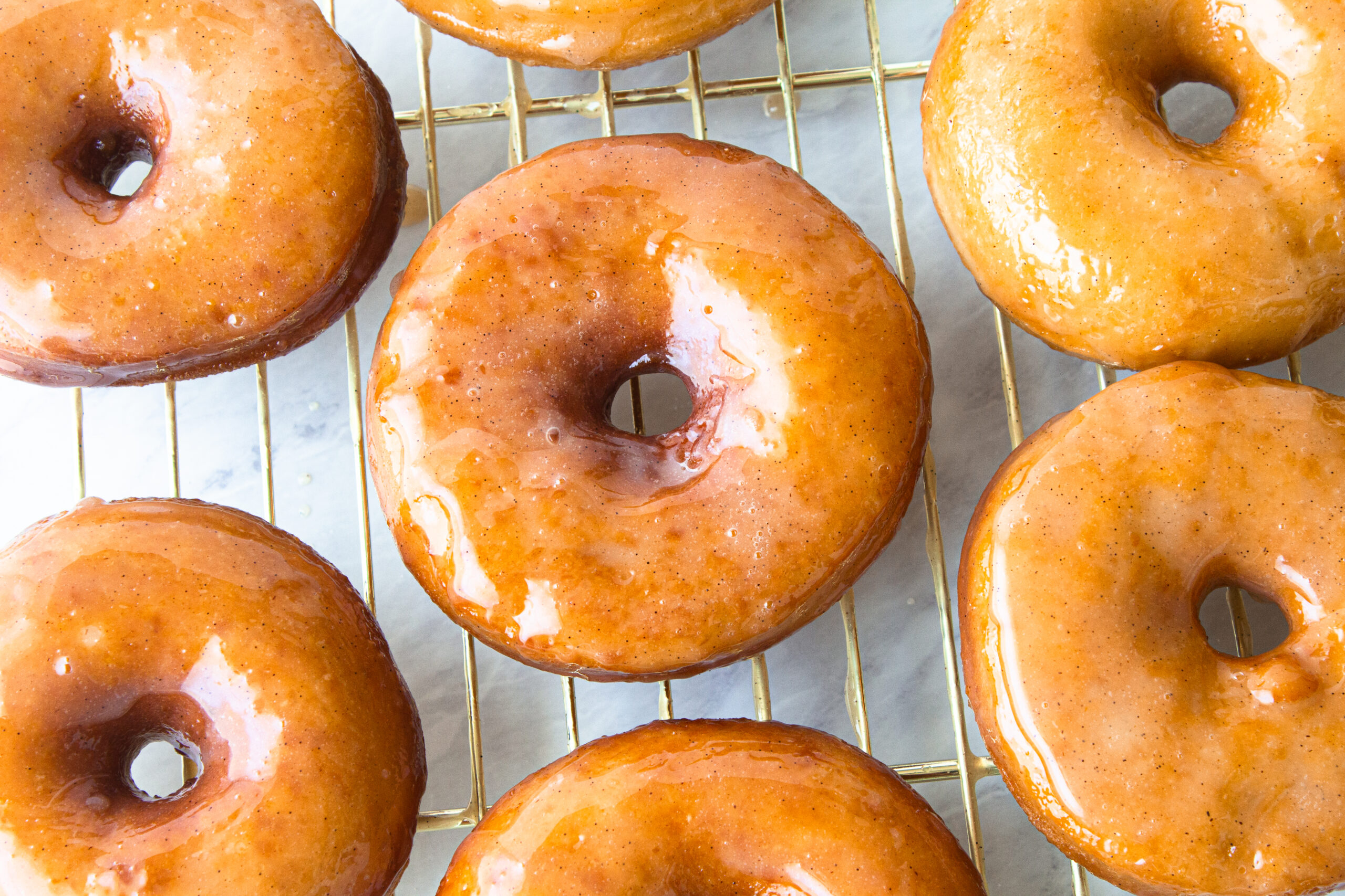 several glazed sourdough donuts on a gold cooling rack