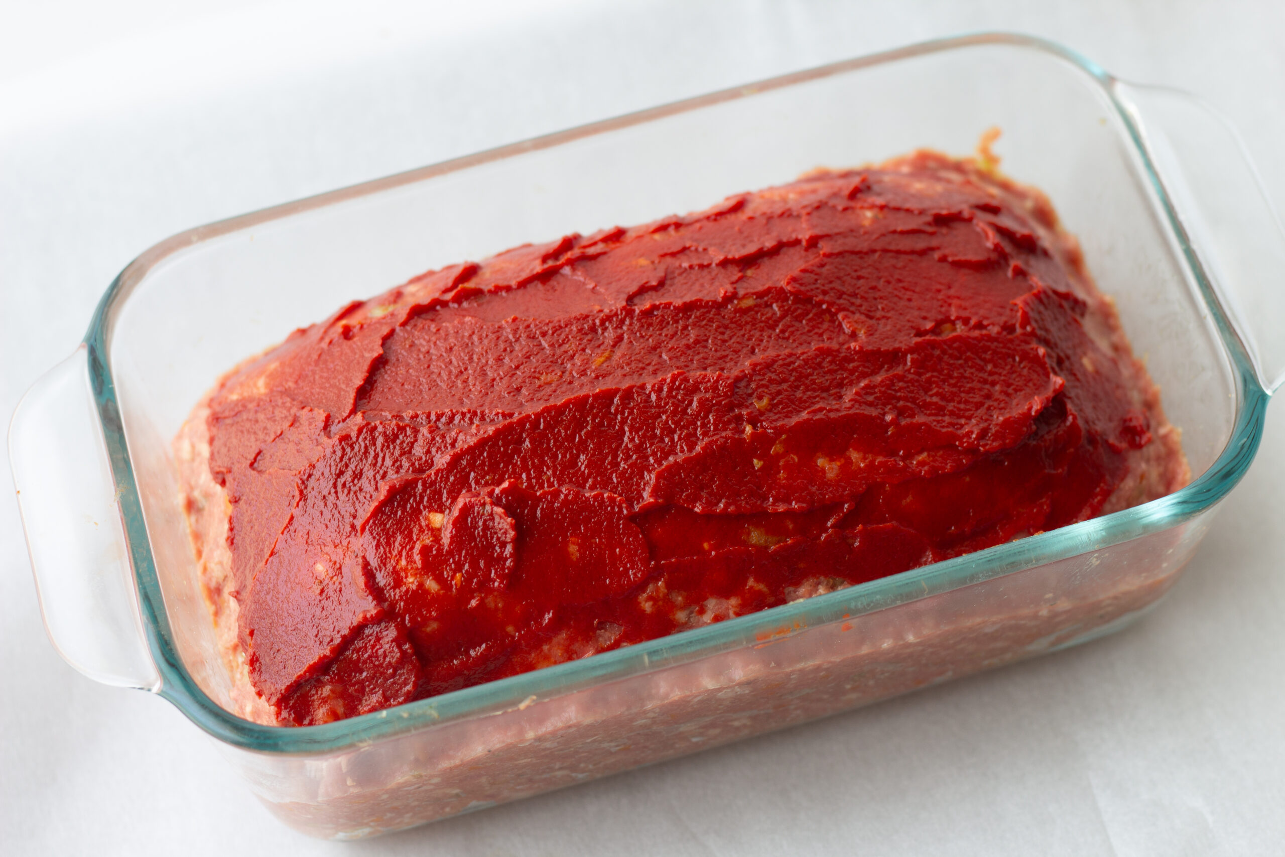 unbaked meatloaf in a baking dish with tomato paste on top