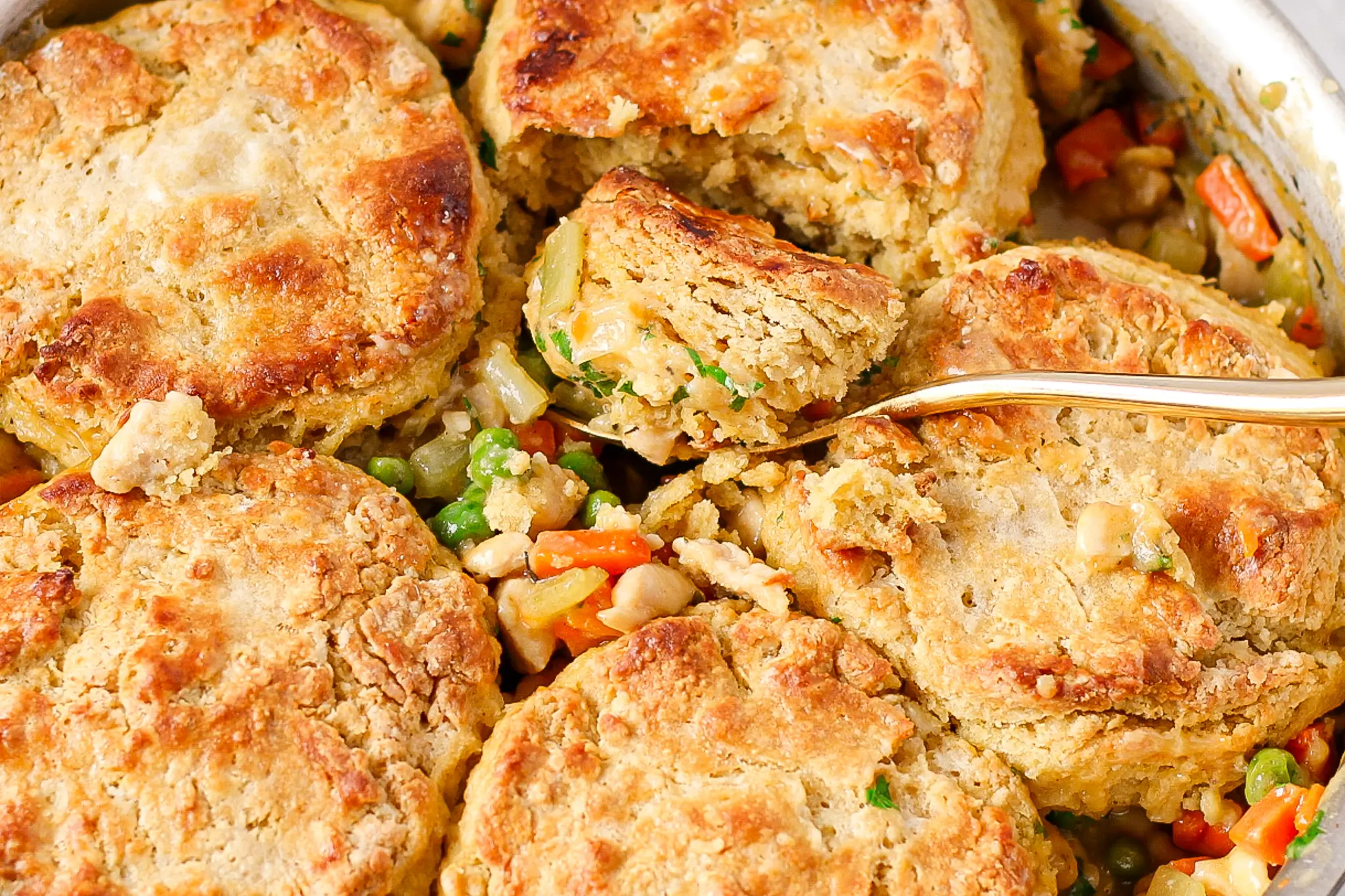 spoon cutting into golden brown biscuit topping