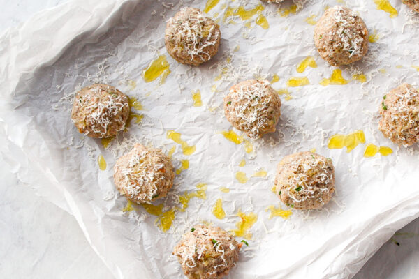 par-cooked meatballs on a baking sheet with parmesan and olive oil on top