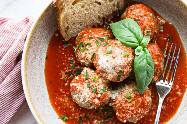 cooked beef pork and veal italian meatballs in a bowl with tomato sauce topped with parmesan and basil with a side of sourdough bread