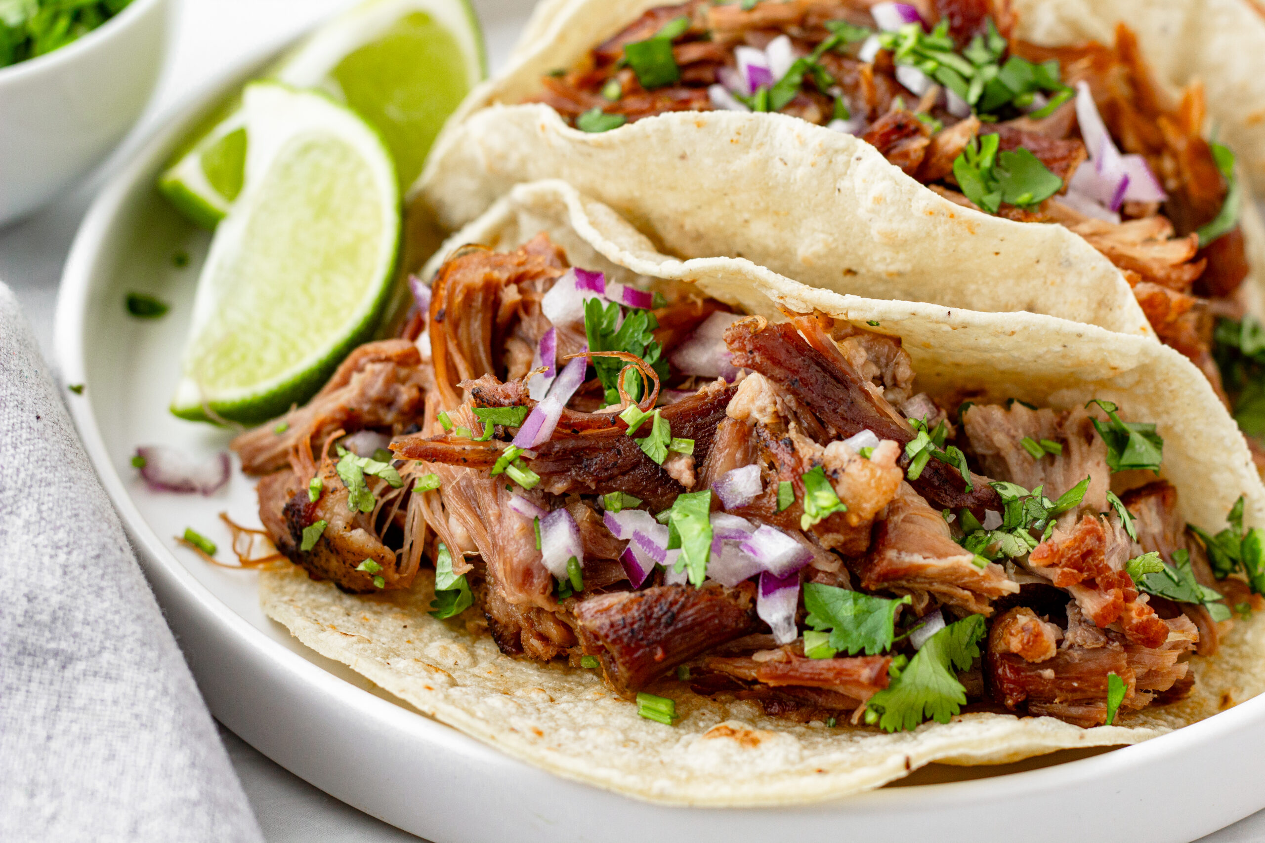 pork carnitas street tacos garnished with red onion and cilantro and a limme wedge