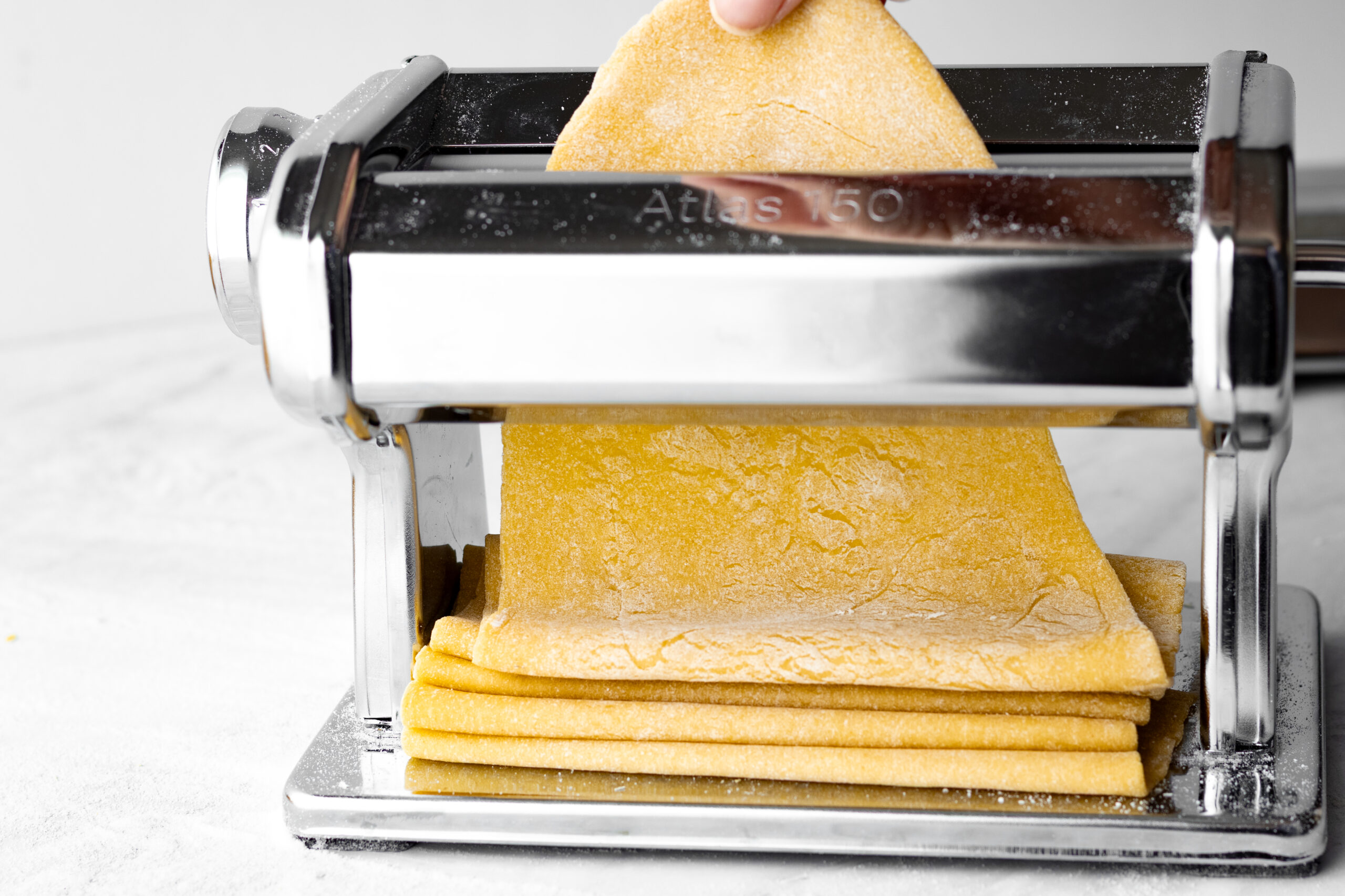 sheet of einkorn pasta being rolled through a pasta machine