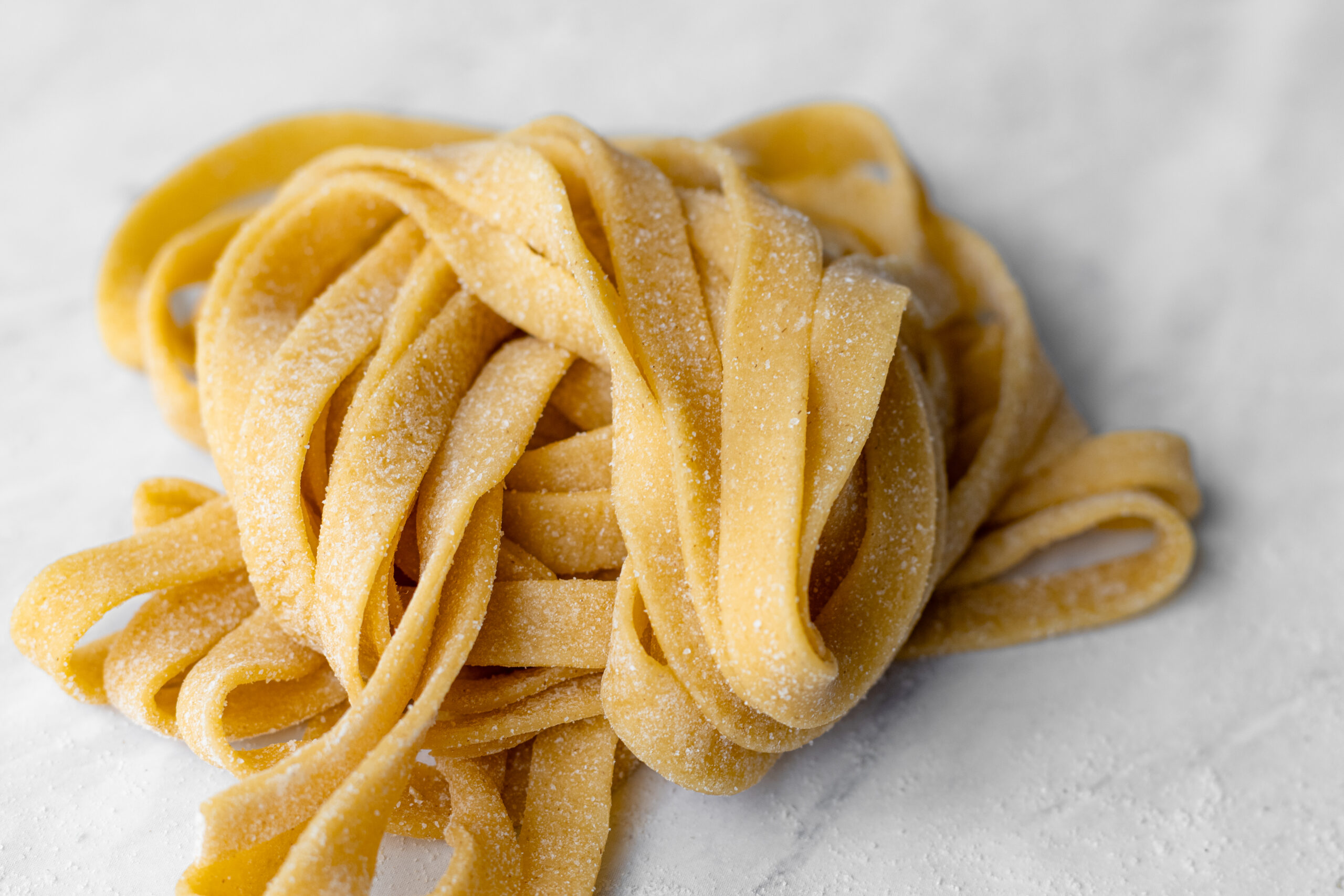 A rustic nest of fresh einkorn pasta fettuccine dusted with flour, piled on a white marble surface