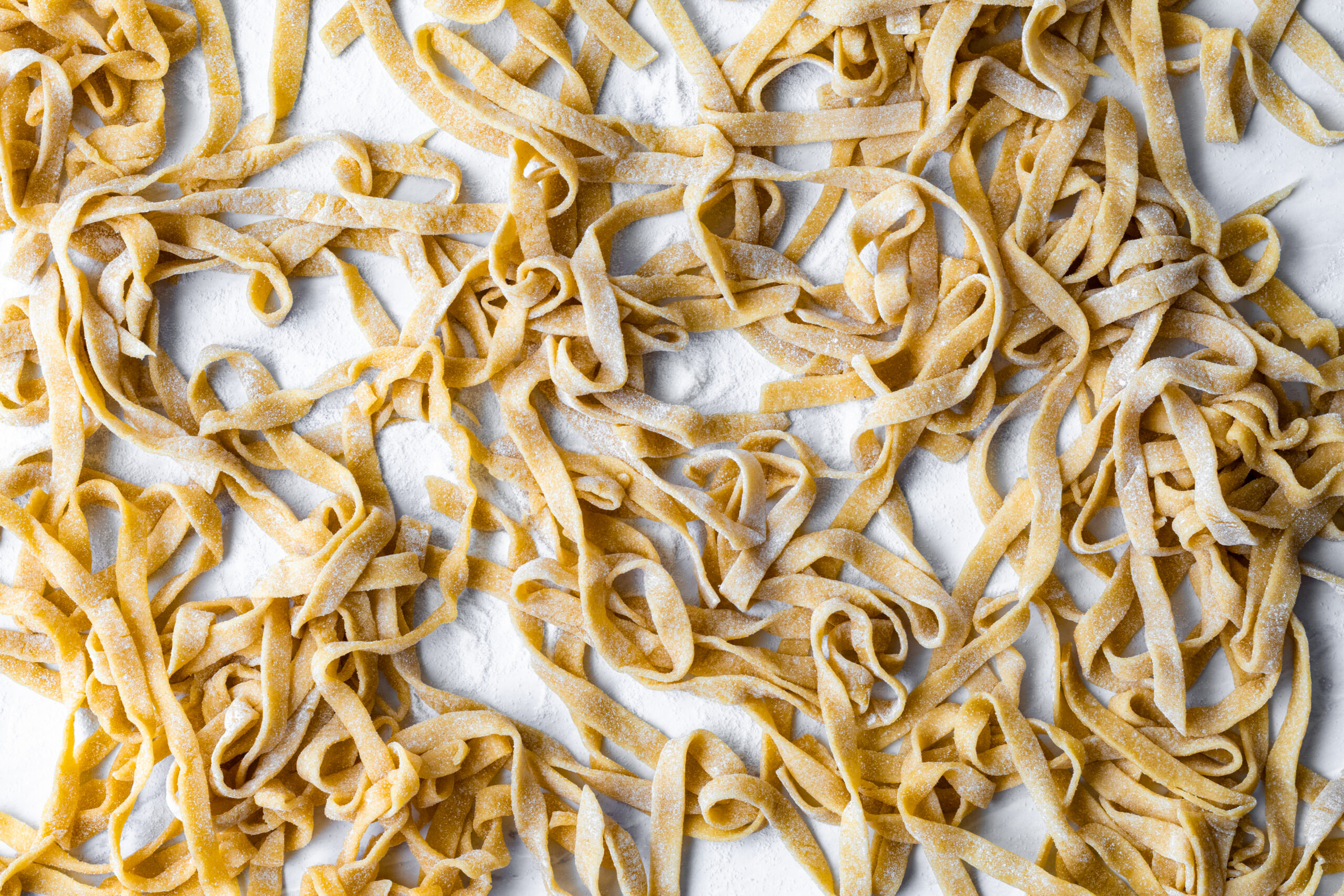 Fresh einkorn pasta fettuccine noodles scattered loosely across a floured white surface after cutting