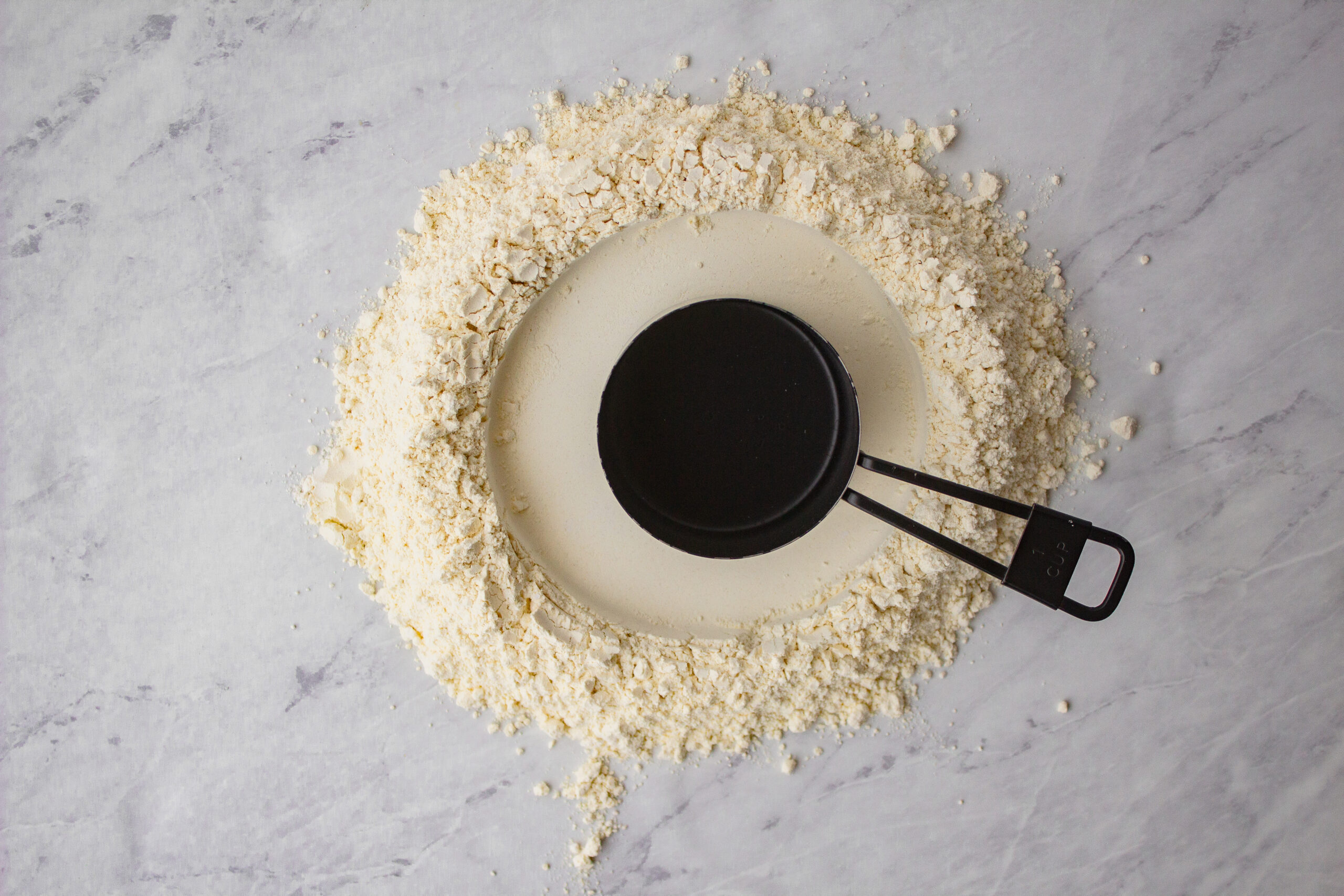 black measuring cup used to make a well out of flour for pasta making
