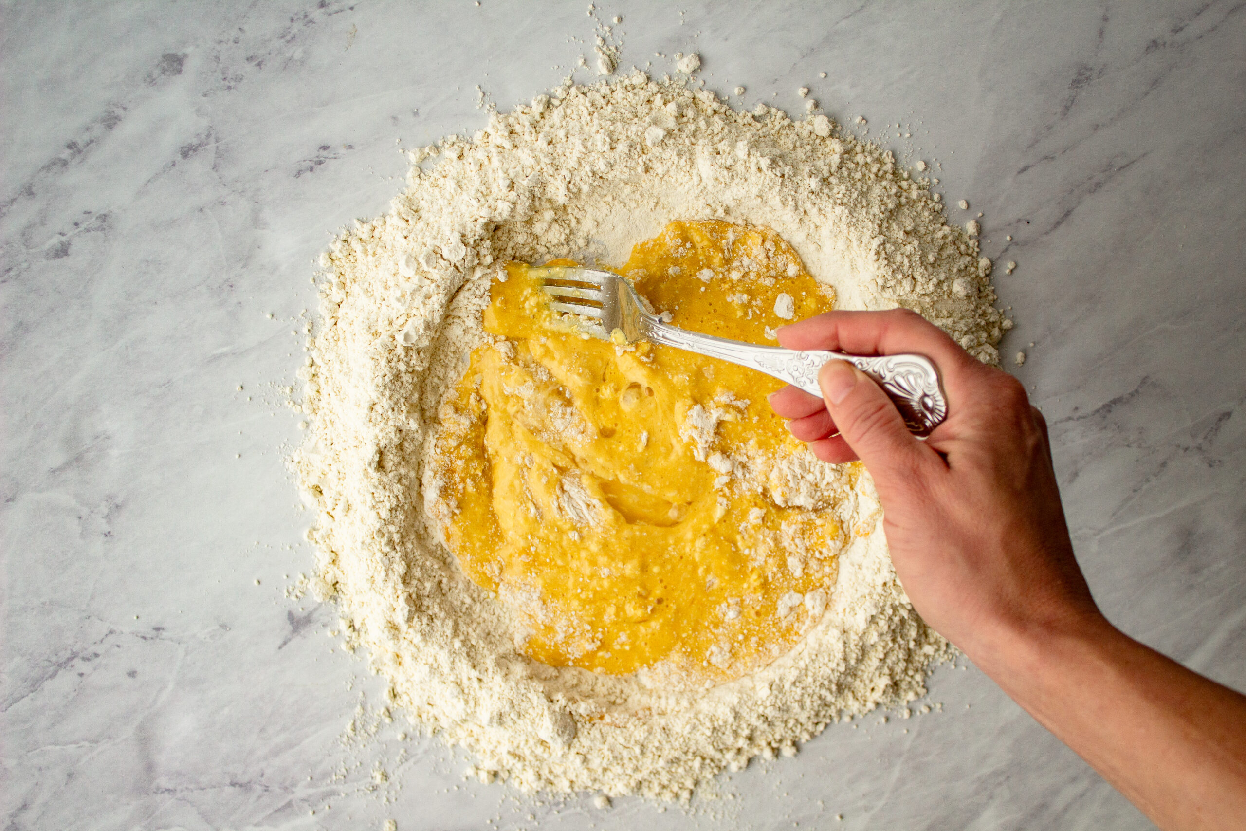 mixing egg yolks into flour with a fork to make pasta dough