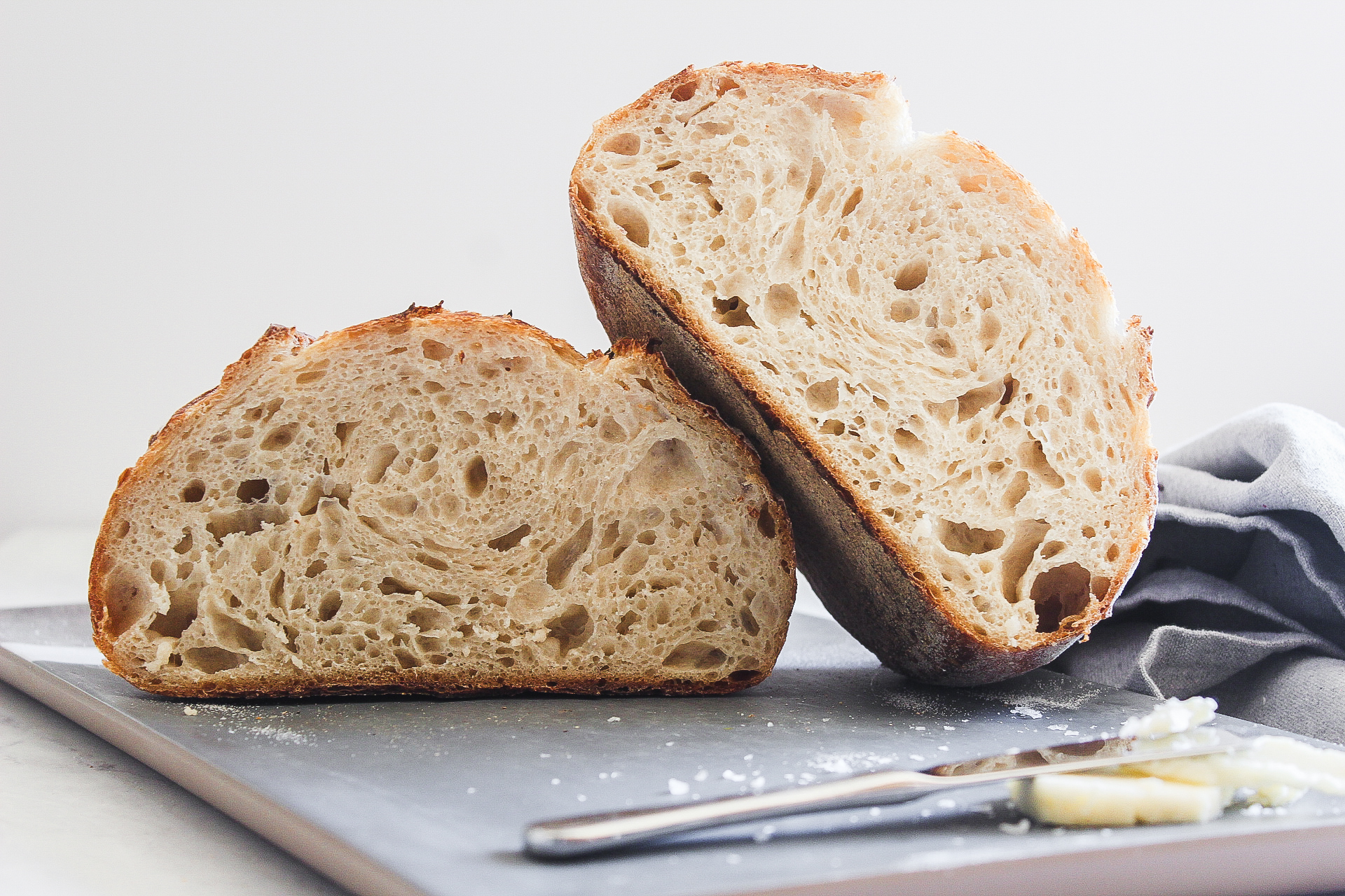 sourdough cut in half and one side resting on top of the other with a butter knife butter and a cutting board