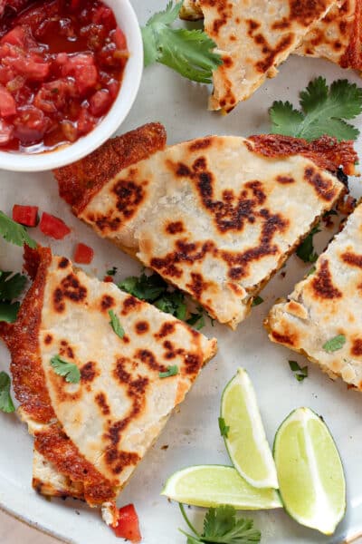 quesadilla cut into fours with a bowl of salsa and lime wedges