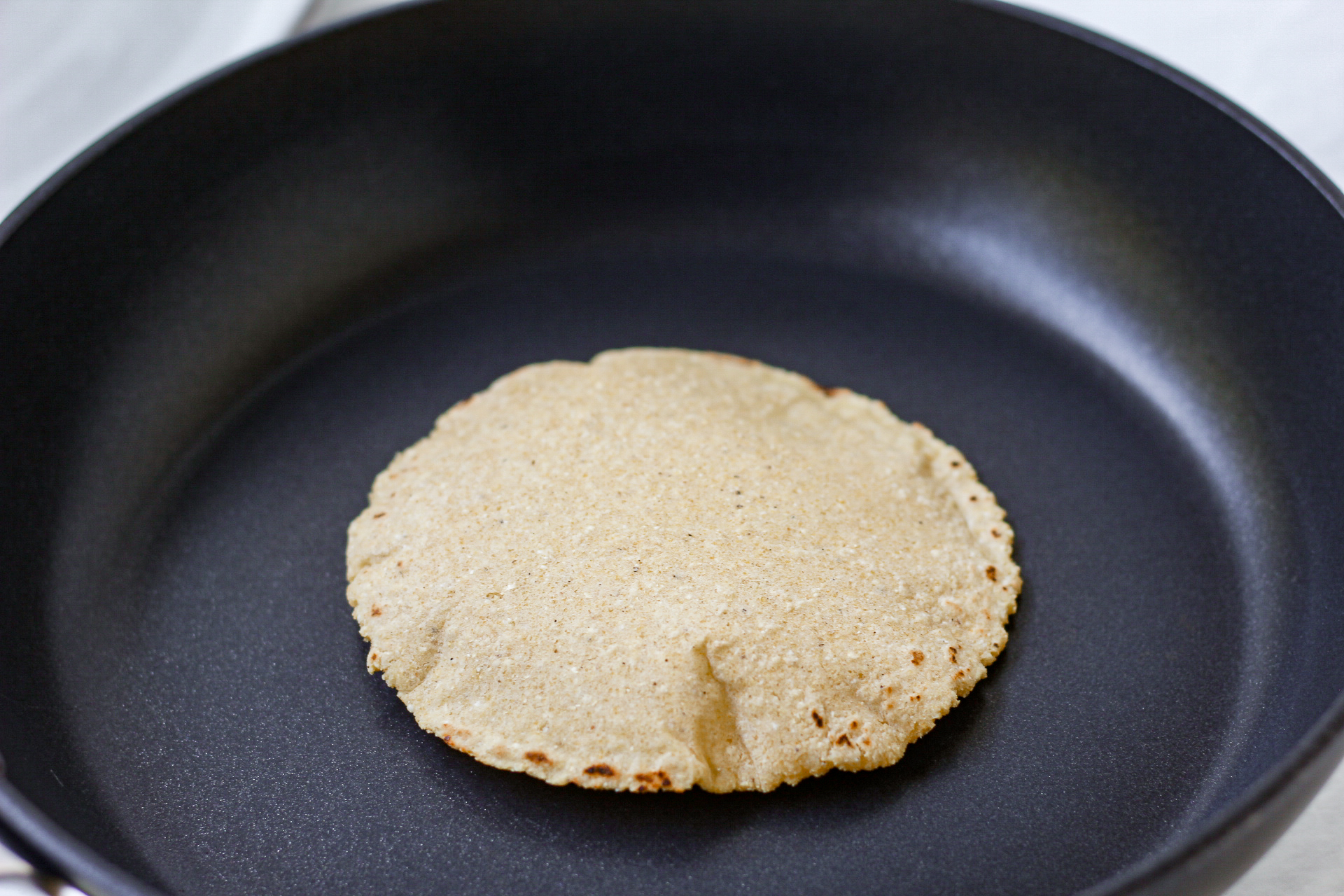 fresh corn tortilla puffed up during the cooking process in a skillet