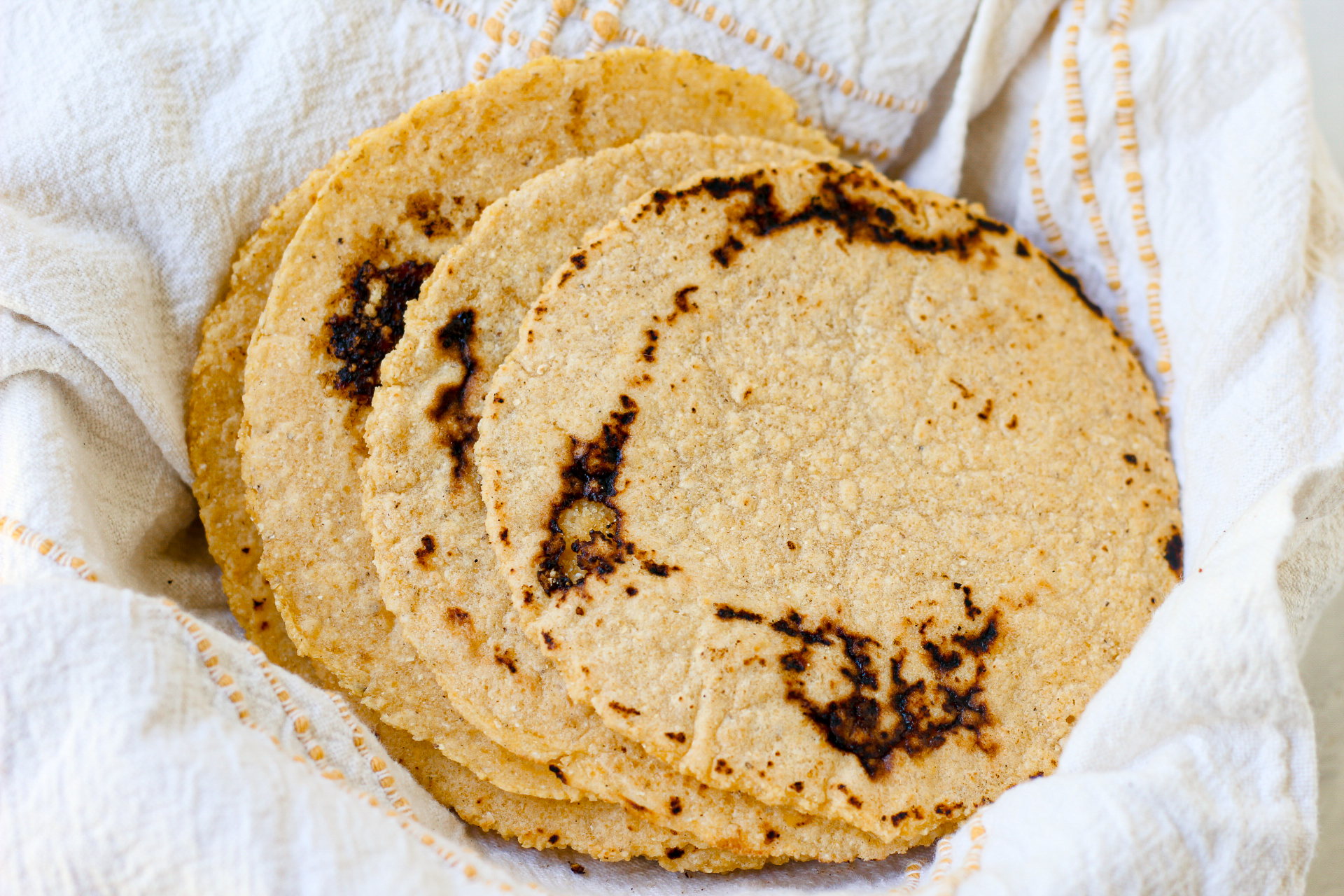 a pile of freshly made corn tortillas in a basket with a towel