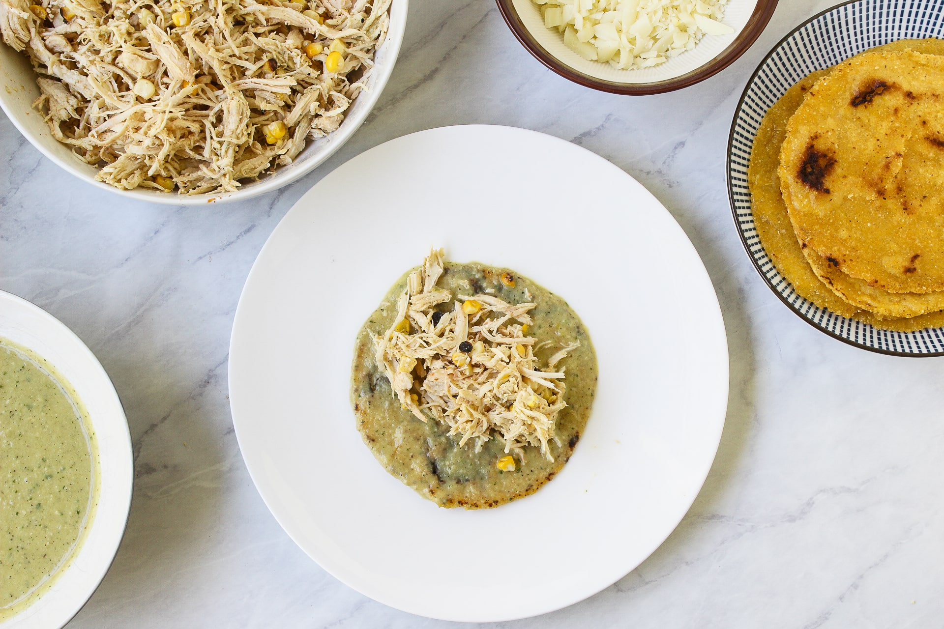 above shot of enchiladas being assembled with shredded chicken salsa verde cheese and tortillas