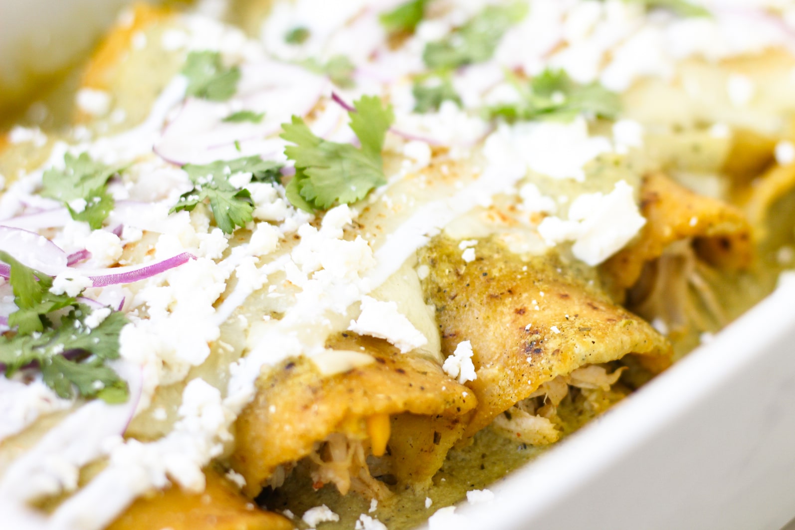close up of baked chicken enchiladas with sour cream red onion and  cilantro on top