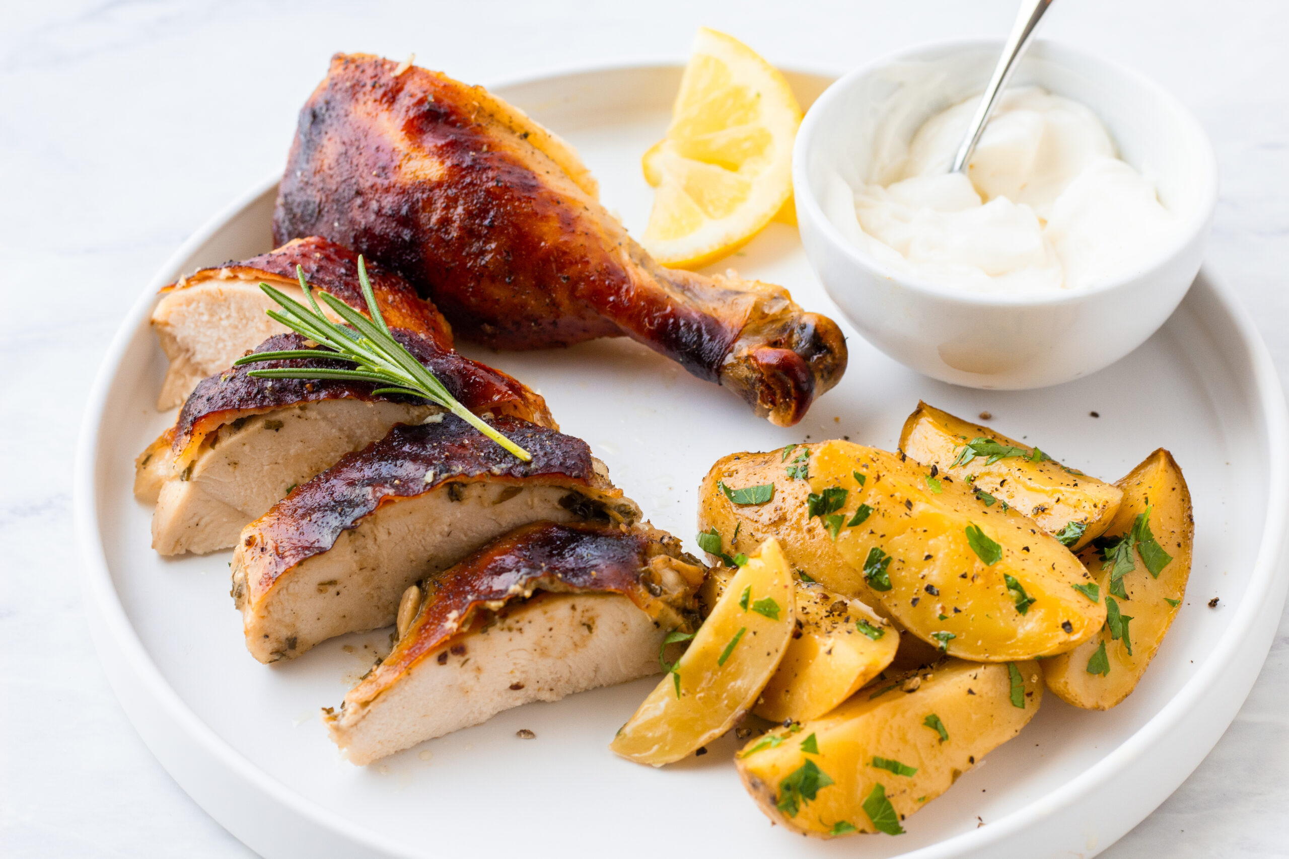 roasted chicken breast and leg displayed on a white plate with roasted potatoes and parsley flakes and a side of horseradish sourcream