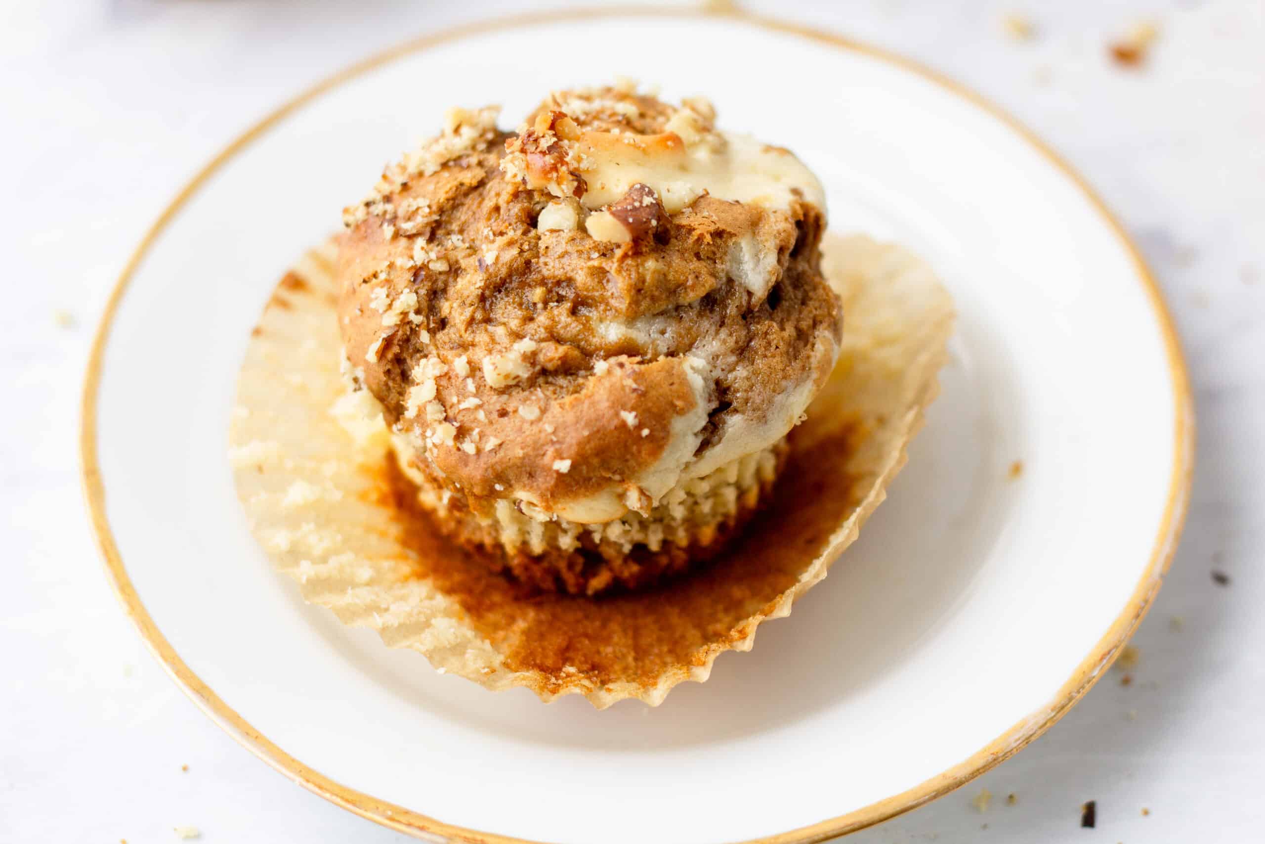 einkorn banana nut cream cheese muffin with wrapper undone on top of a small white plate with a gold rim