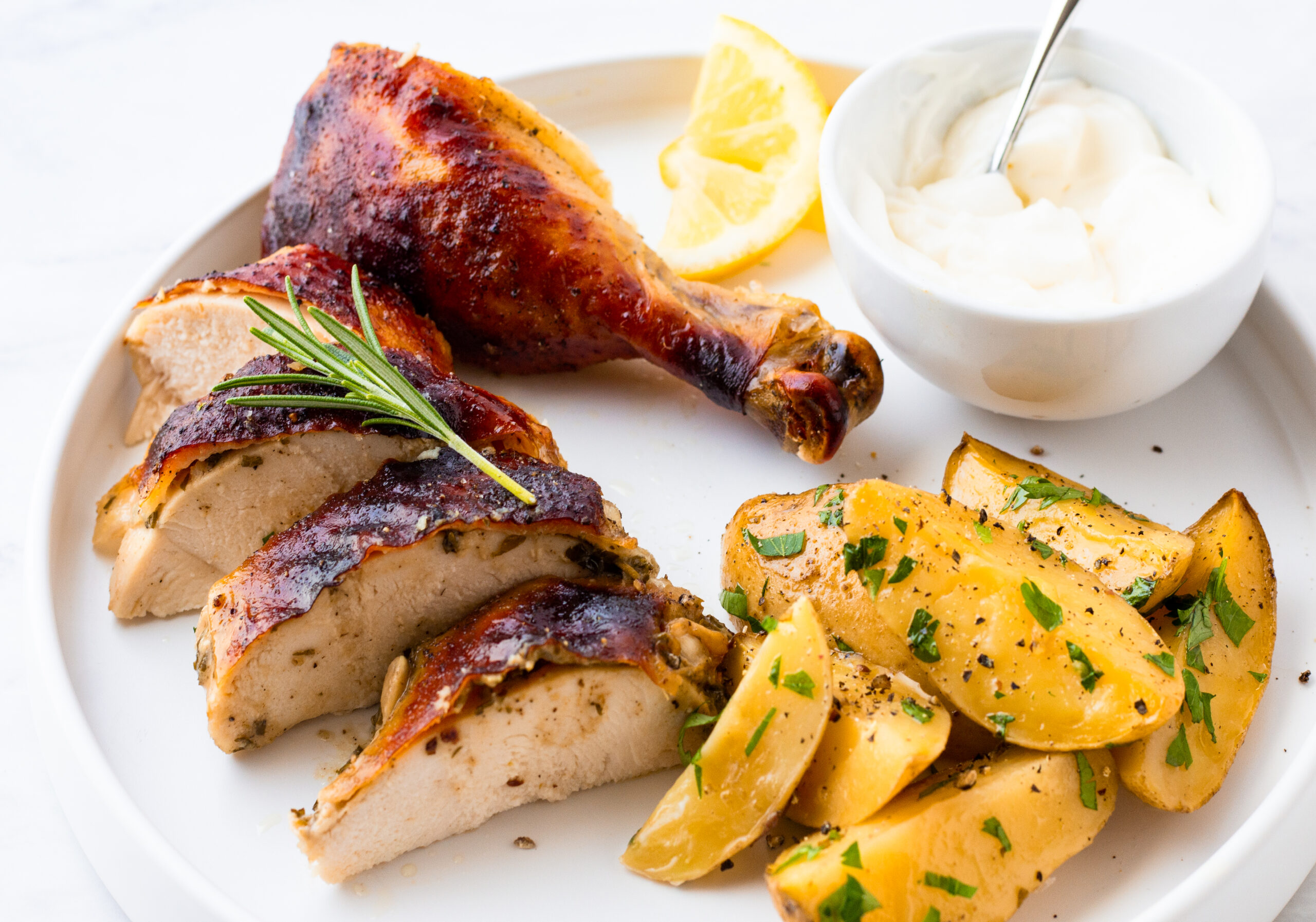 roasted chicken breast and leg displayed on a white plate with roasted potatoes and parsley flakes and a side of horseradish sourcream