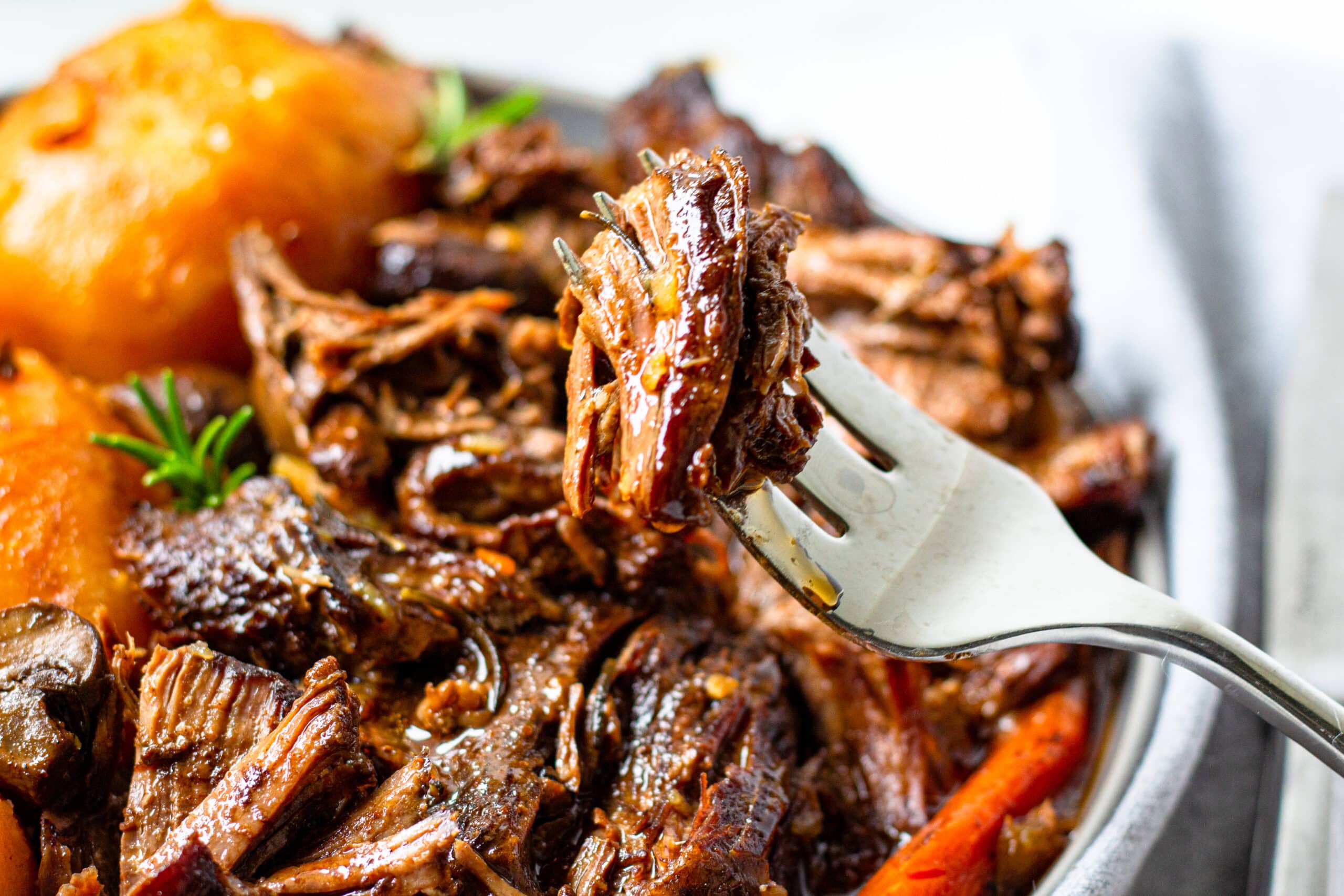 fork with tender pot roast beef on it above a plate