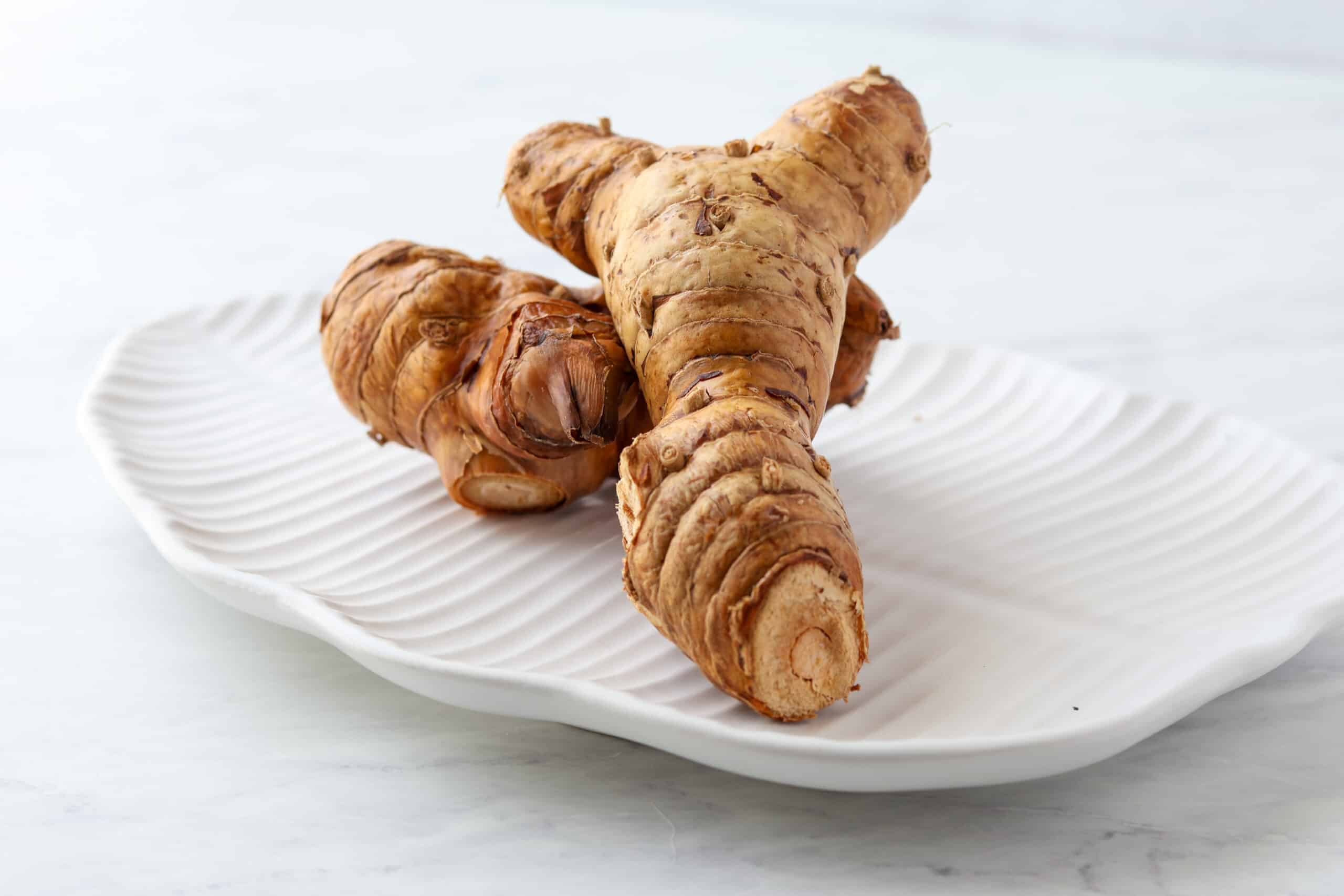 Fresh galangal root on a white ceramic plate, a key ingredient in Tom Kha Gai Thai coconut soup