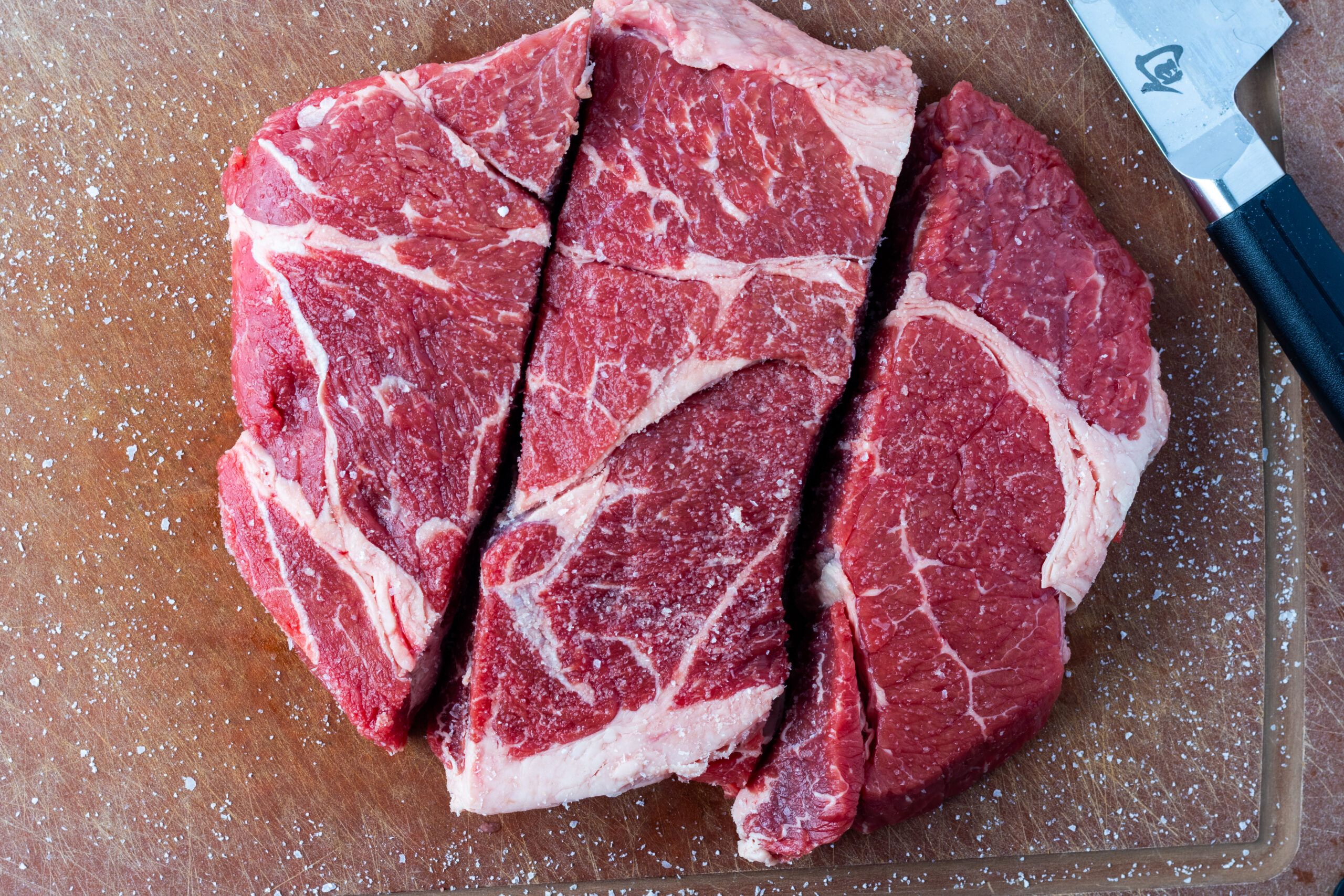 Three pieces of raw chuck roast pre-salted or dry brined on a wooden cutting board for beef tinga recipe