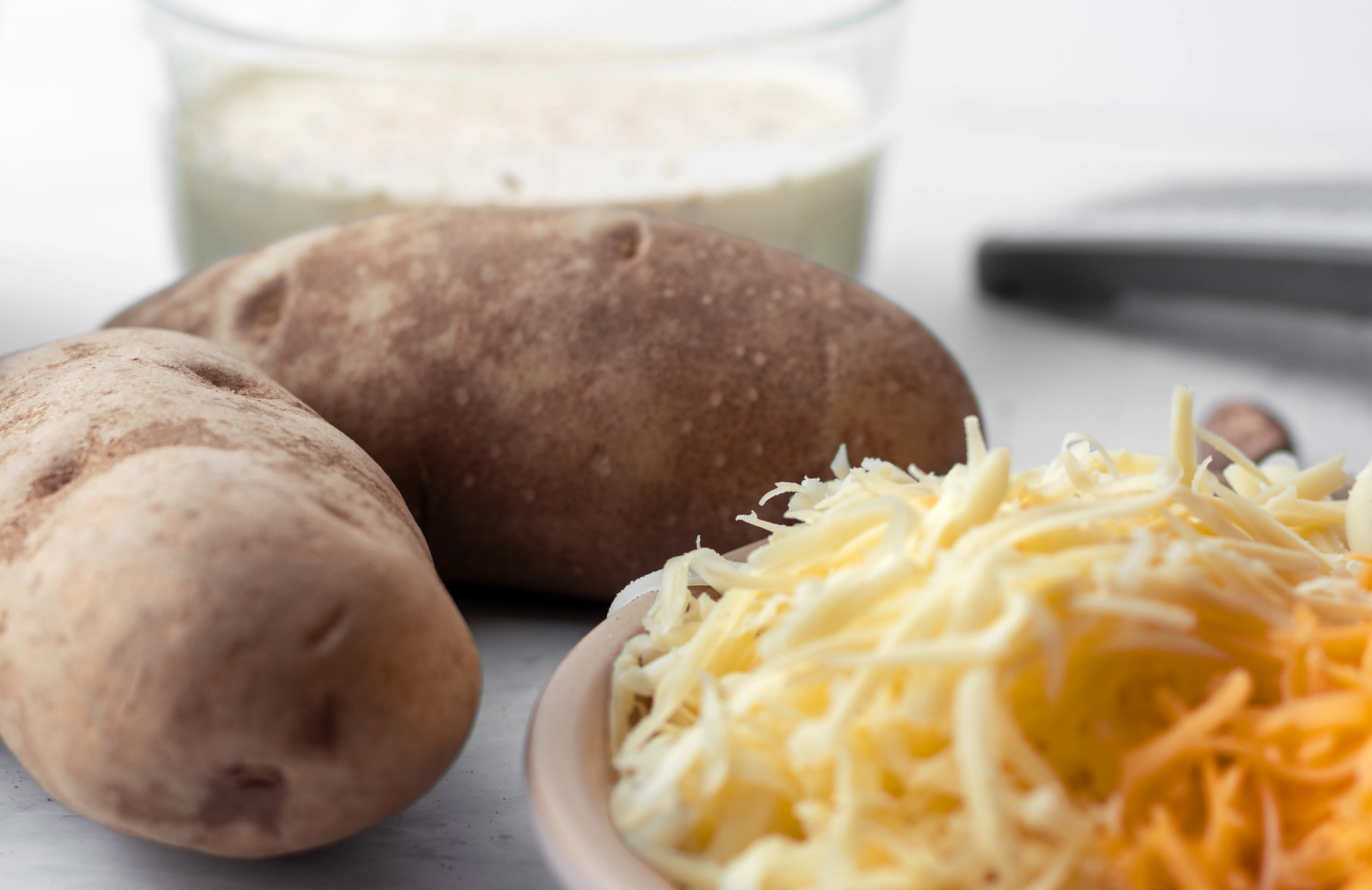 Russet potatoes, hand shredded gruyere and cheddar, heavy cream, and a mandoline on a marble surface