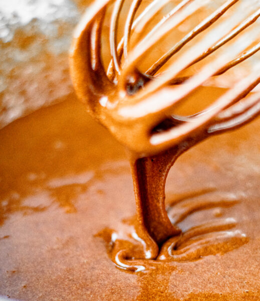 Glossy brownie batter dripping from a whisk showing the rich chocolate texture before baking