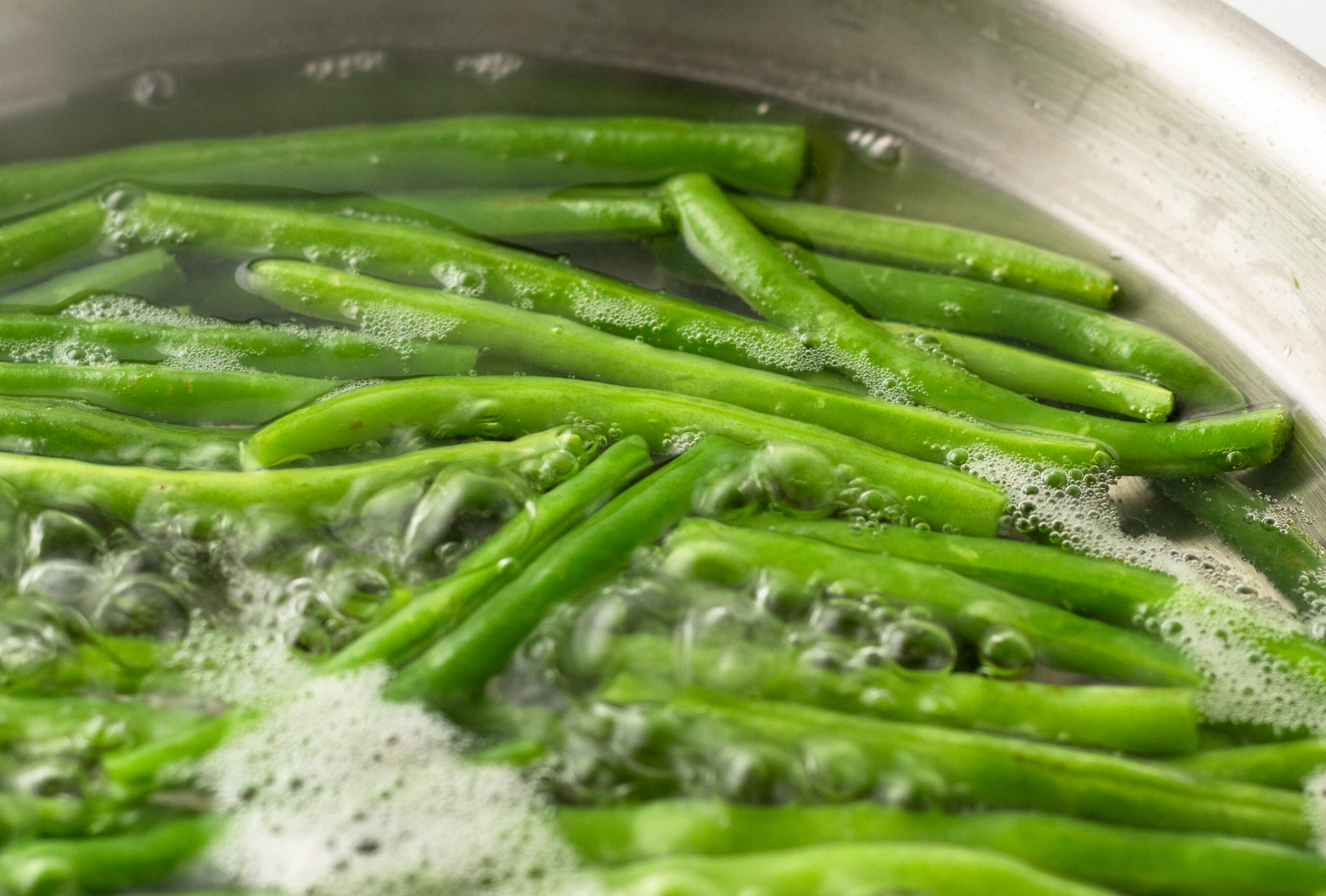 Fresh green beans blanching in generously salted boiling water in a stainless steel pot