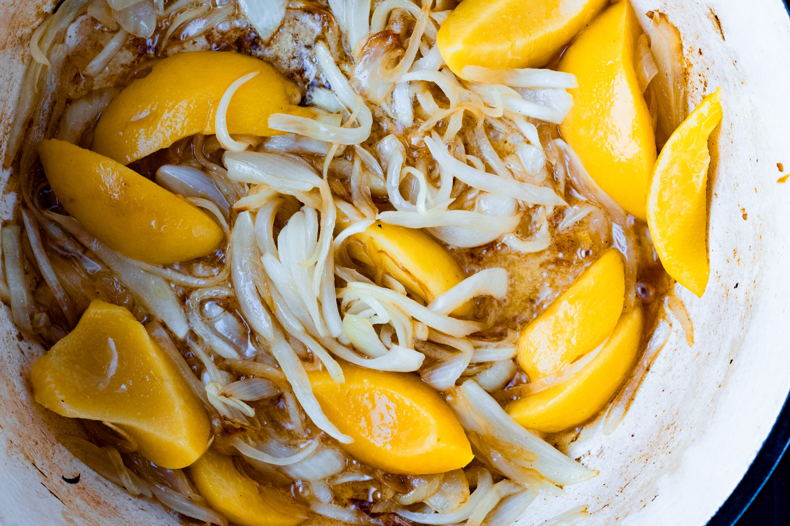 Bright yellow canned peach slices and sweet onion strips in a dutch oven with savory braising liquid