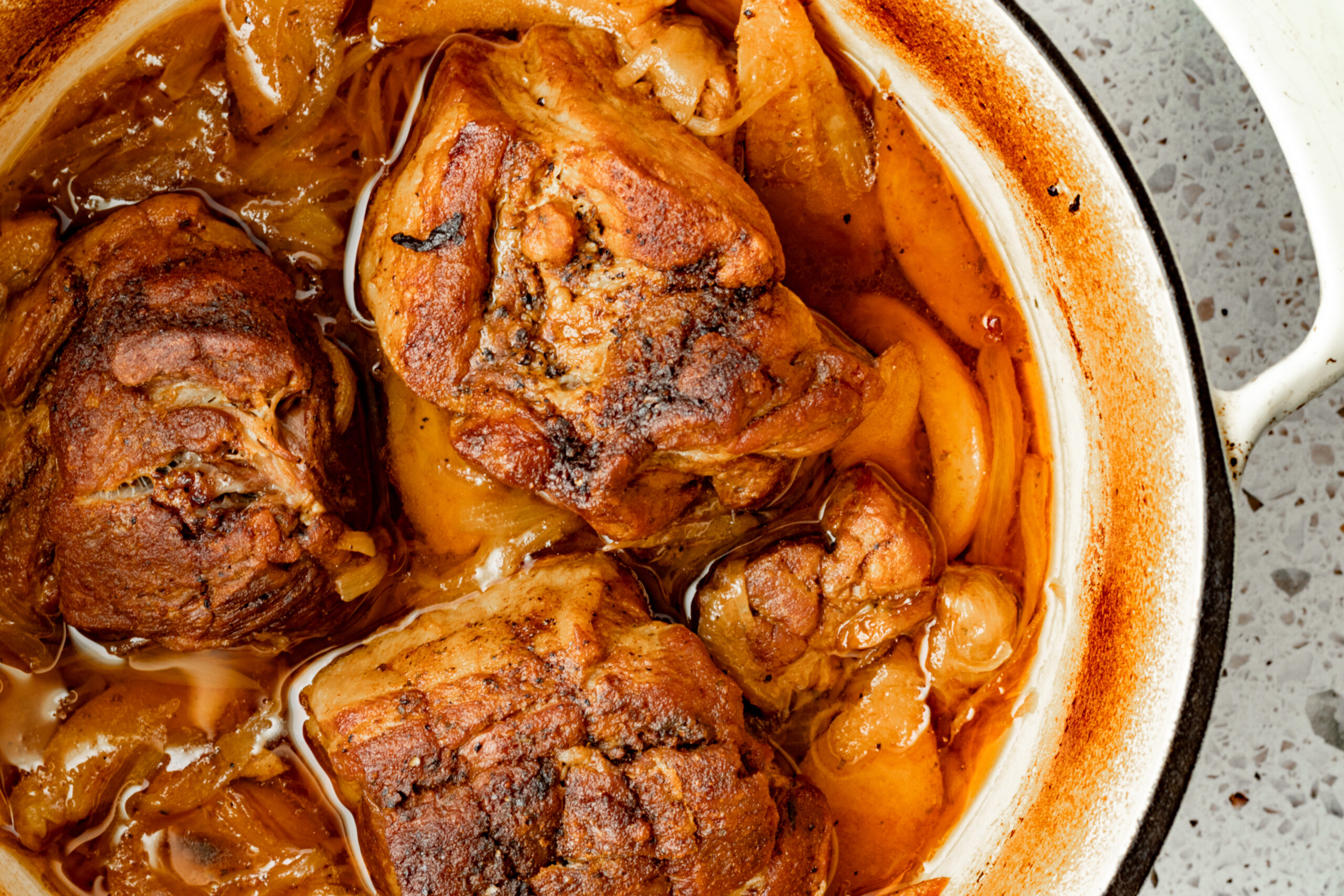 Three pieces of pork shoulder braised in beer with caramelized onions and peaches in a cream enameled dutch oven