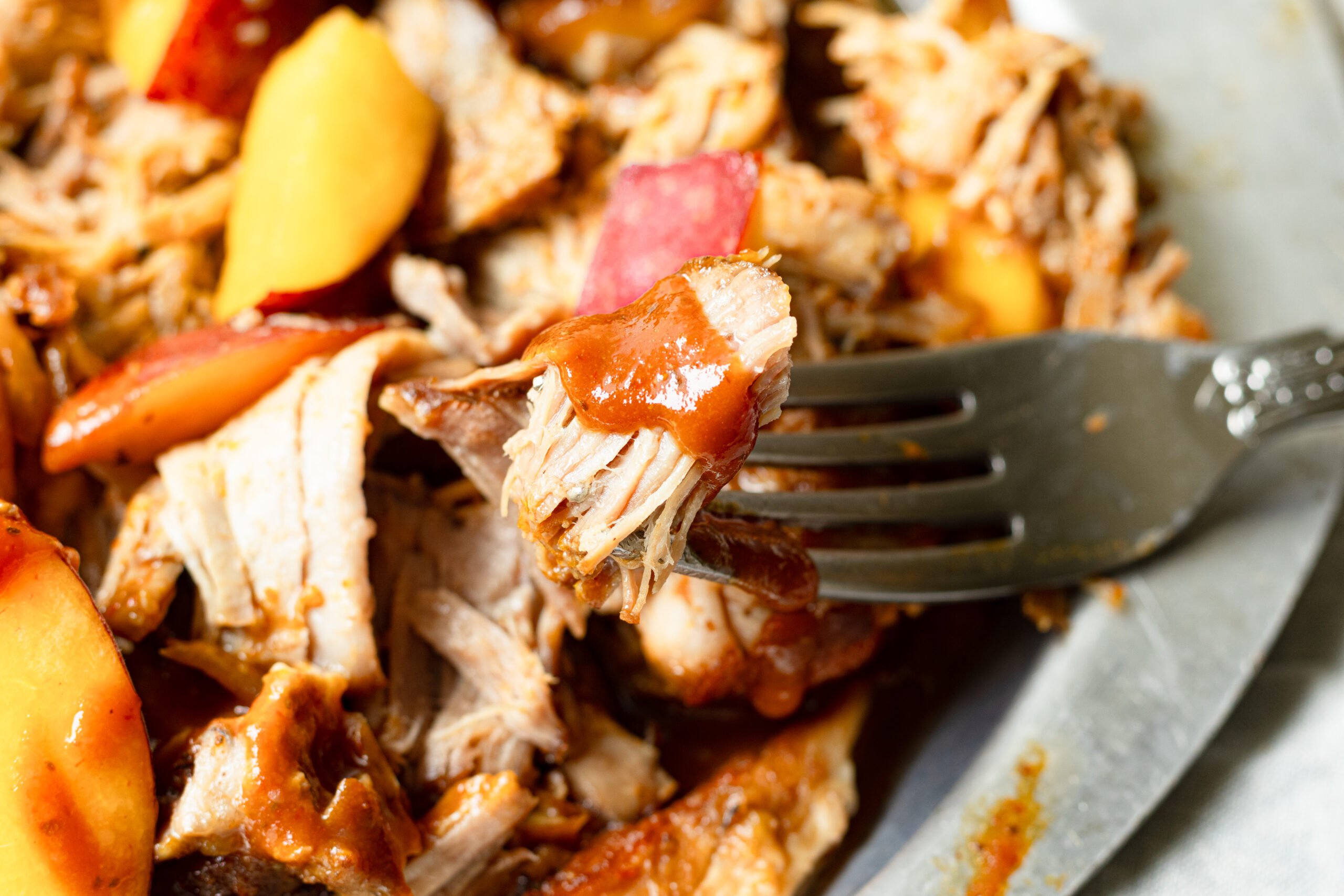 A forkful of tender shredded pulled pork with BBQ sauce and a fresh peach slice up close