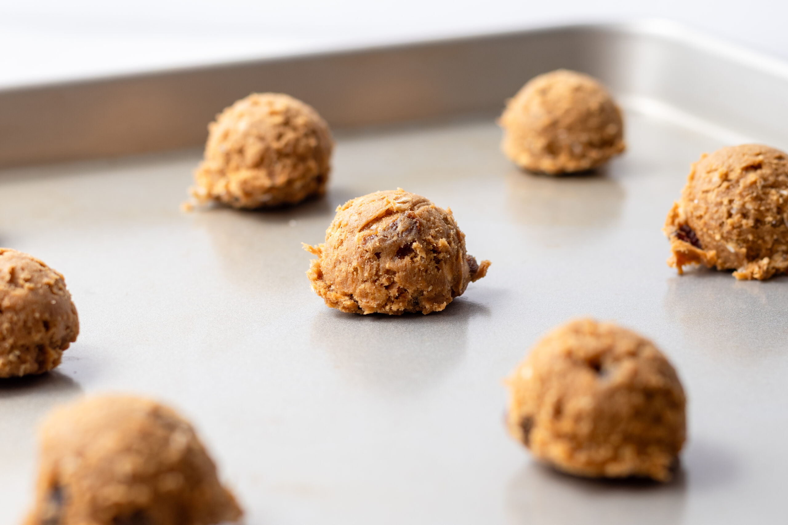 Scooped einkorn oatmeal raisin cookie dough balls on a silver baking sheet ready to bake