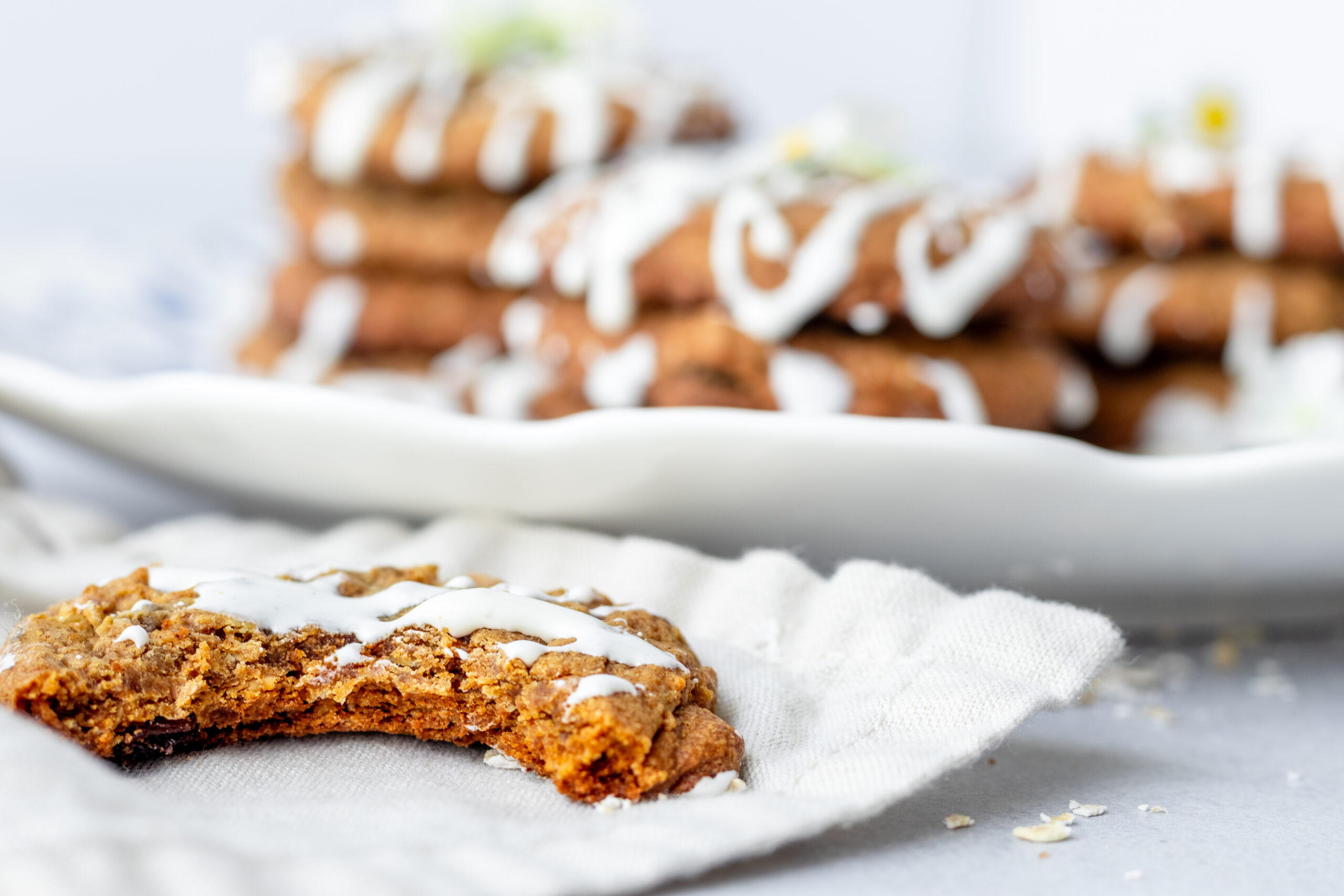 Halved iced einkorn oatmeal raisin cookie on a linen napkin showing soft chewy interior with marshmallow drizzle and cookies stacked on a white plate in the background