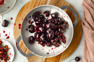 Fresh pitted dark sweet cherries in a silver pan on a wooden cutting board