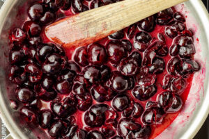 Dark sweet cherries simmering in a pot with a wooden spoon