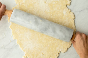Hands rolling out einkorn pie dough with a marble rolling pin on a floured surface