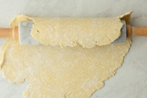 Einkorn pie dough draped over a marble rolling pin being transferred to a pie dish